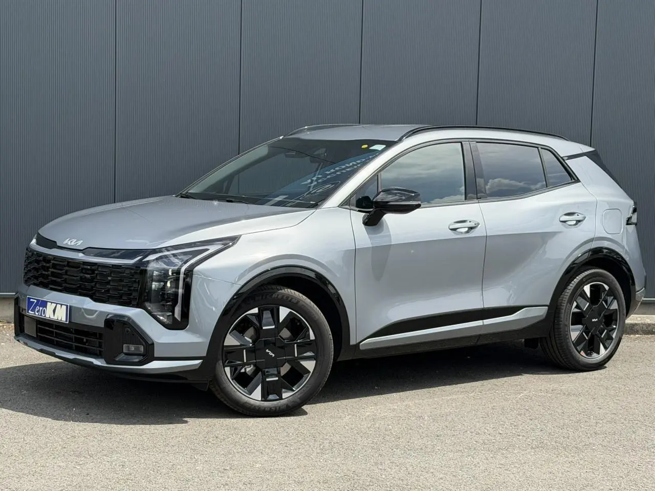KIA SPORTAGE gris lunaire en vue 3/4 avant droit, avec jantes alliage noires et toit noir contrasté.