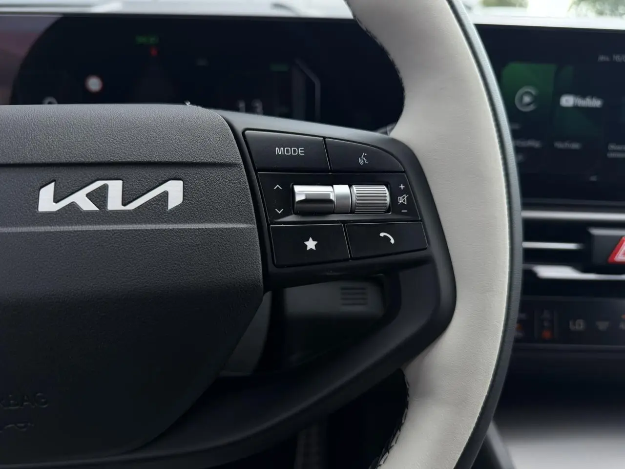 Gros plan sur le volant bi-ton clair du Kia Sportage 2026 avec commandes multifonctions à droite et logo Kia visible.