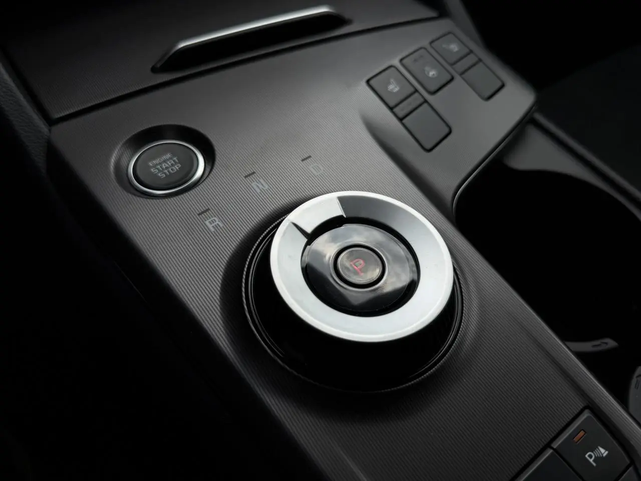 Gros plan sur la molette de sélection de vitesse et bouton start/stop dans l’habitacle noir du Kia Sportage gris lunaire.