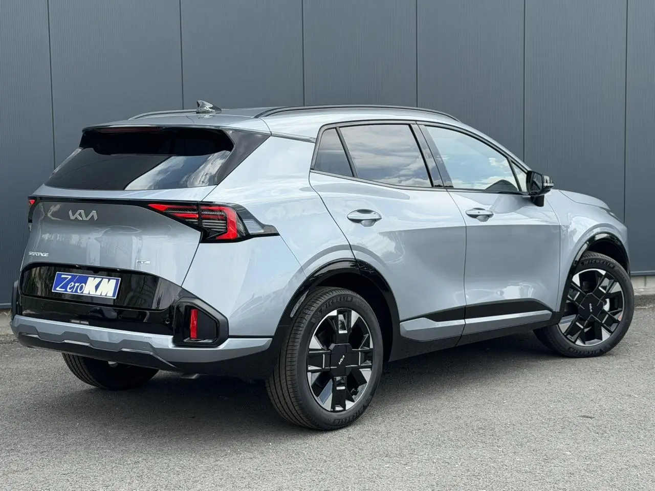 KIA SPORTAGE 2026 gris lunaire en 3/4 arrière droit, avec jantes alliage noires et feux arrière LED distinctifs.