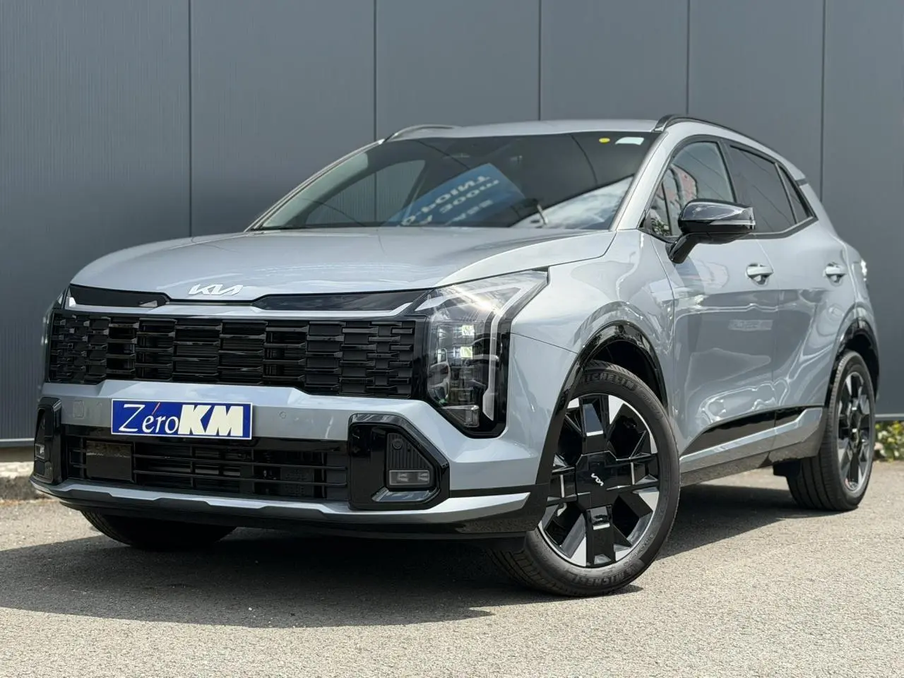 KIA SPORTAGE gris lunaire en 3/4 avant droit avec calandre noire et jantes alliage noires distinctives.