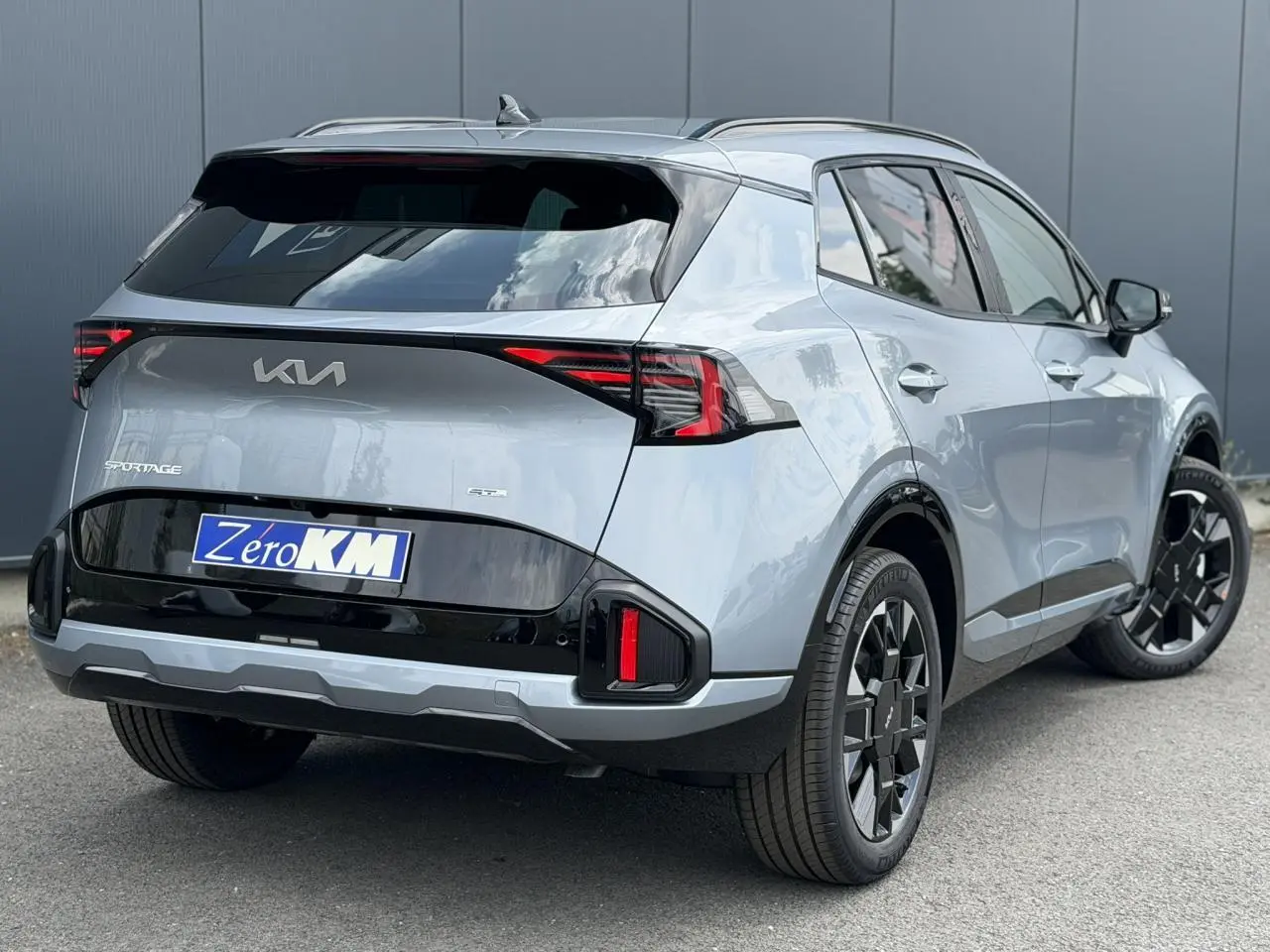 Vue 3/4 arrière droite du KIA Sportage gris lunaire 2026 avec jantes alliage noires et feux arrière LED distinctifs.