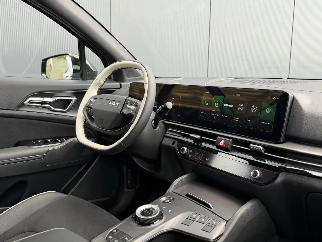 Vue intérieure côté conducteur du Kia Sportage 2026, volant bi-ton et écran tactile large sur tableau de bord noir.