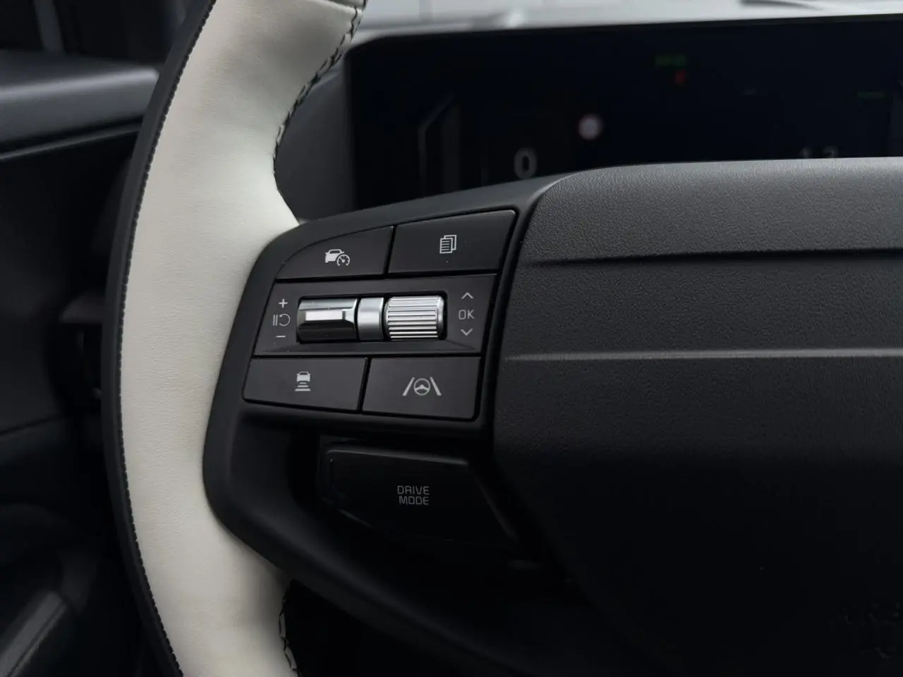 Gros plan sur les commandes gauche du volant bi-ton cuir blanc et noir du Kia Sportage 2026 gris lunaire.