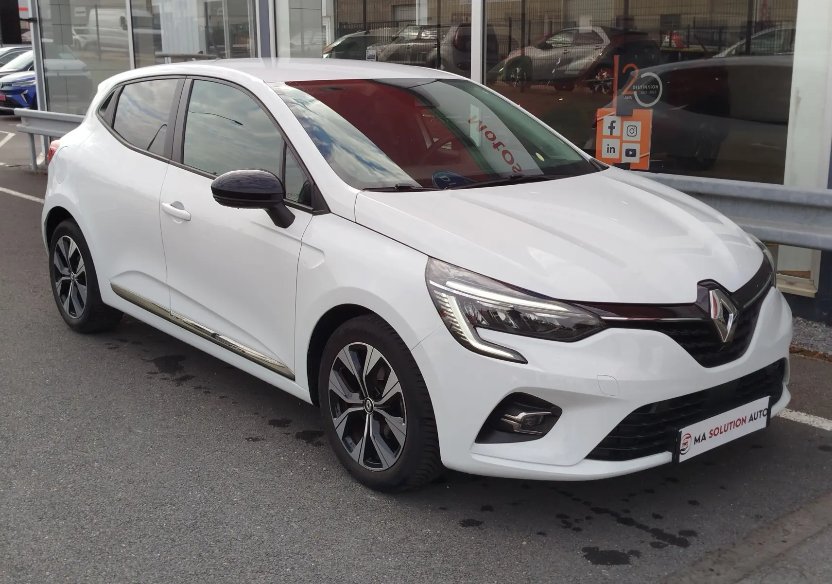Renault Clio blanc glacier vue 3/4 avant droit, avec jantes alliage et feux LED distinctifs.