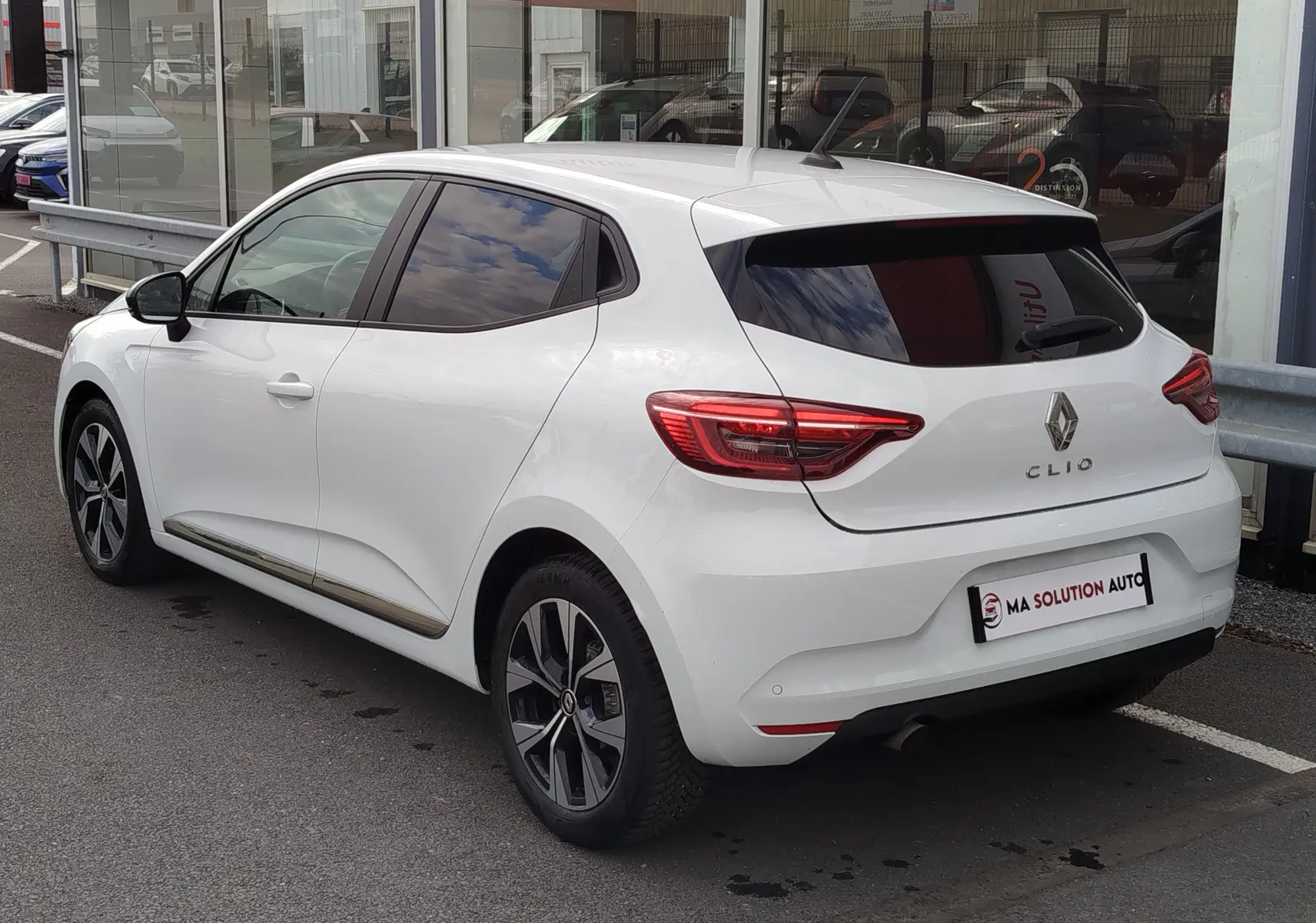 Vue 3/4 arrière droite d'une Renault Clio blanc glacier 2023 avec jantes alliage et vitres teintées.