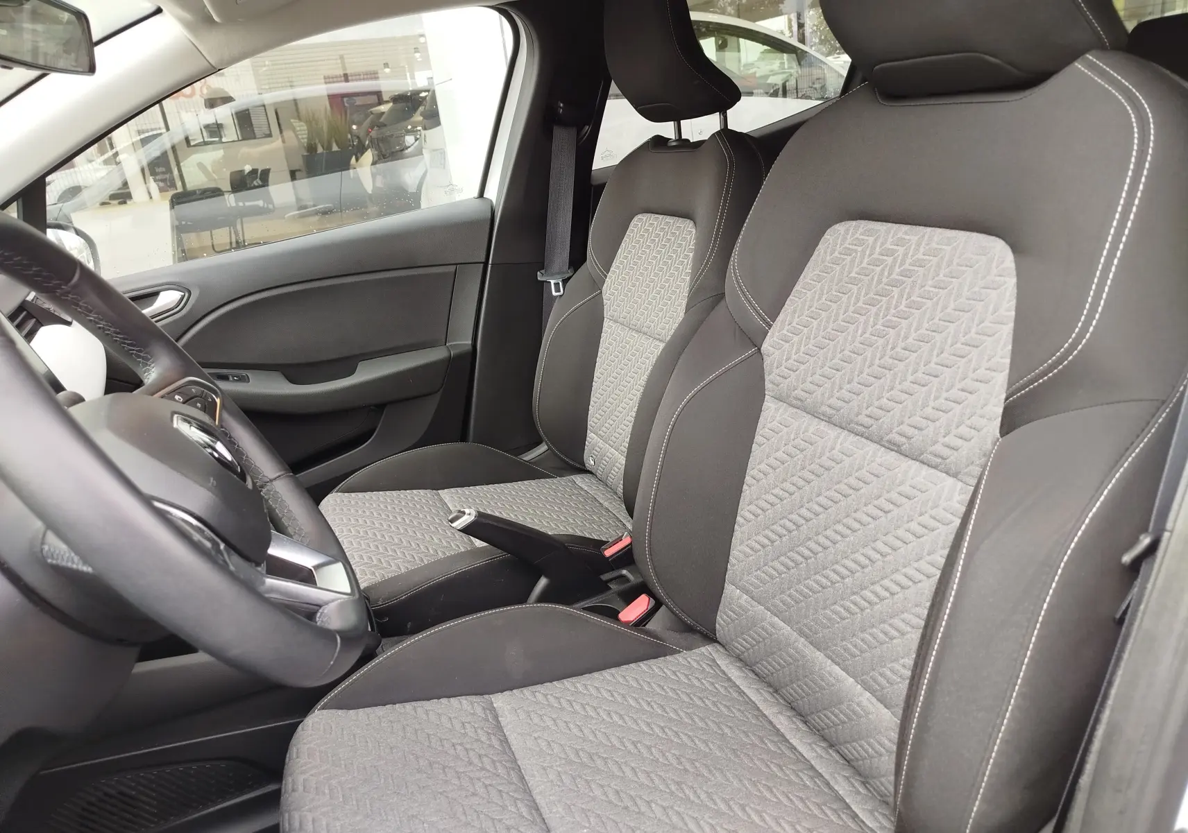 Vue intérieure côté conducteur de la Renault Clio 2023, sièges tissu gris à motifs géométriques et volant cuir noir.