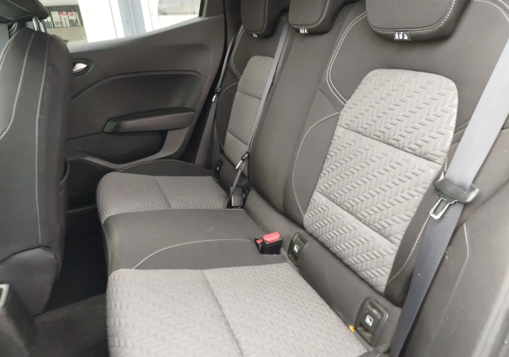 Vue intérieure des sièges arrière gris clair et noir de la Renault Clio 2023, avec ceinture de sécurité et appuie-têtes visibles.