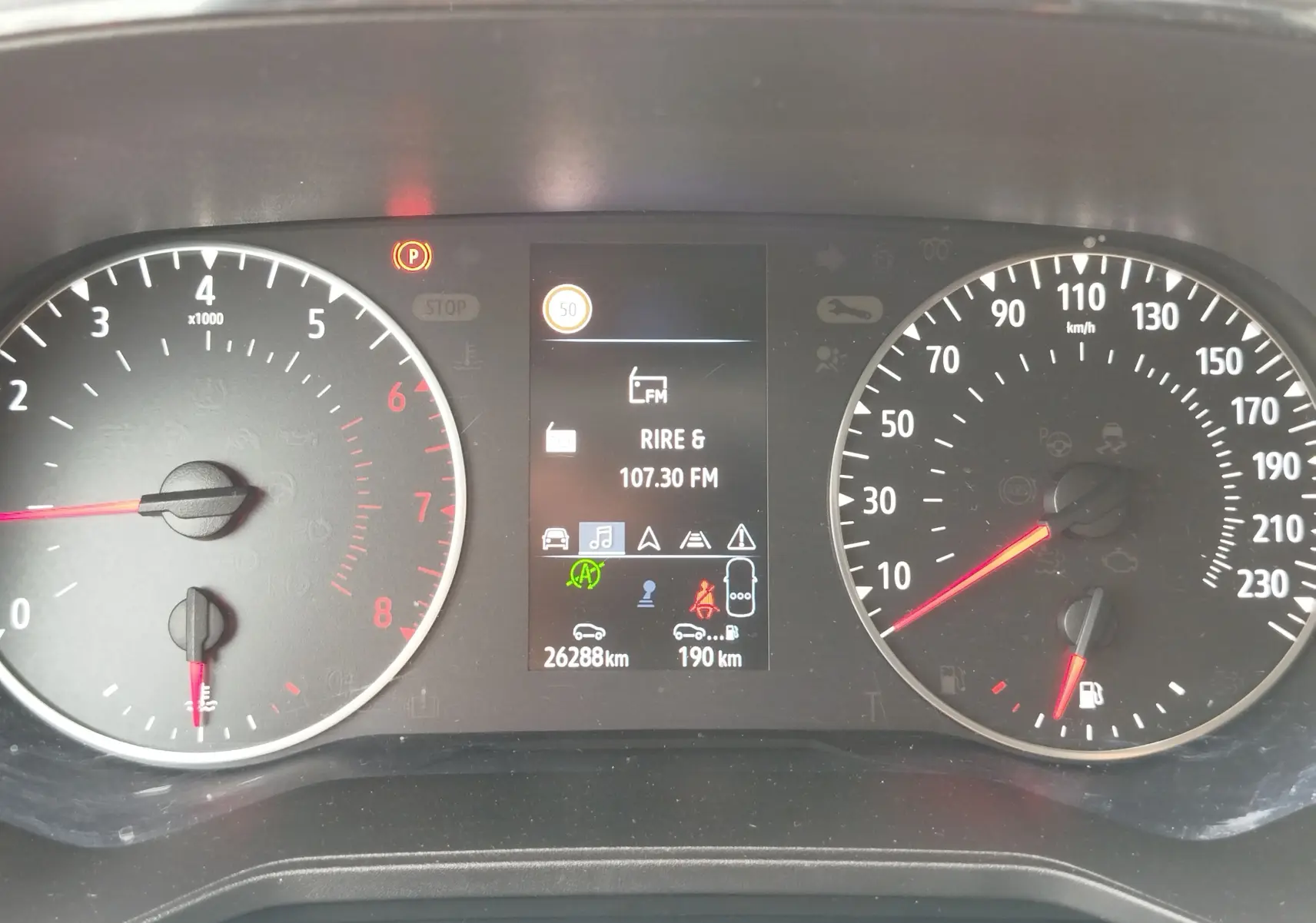 Tableau de bord de Renault Clio 2023, affichage central numérique avec compte-tours et vitesse en km/h, témoin parking allumé.