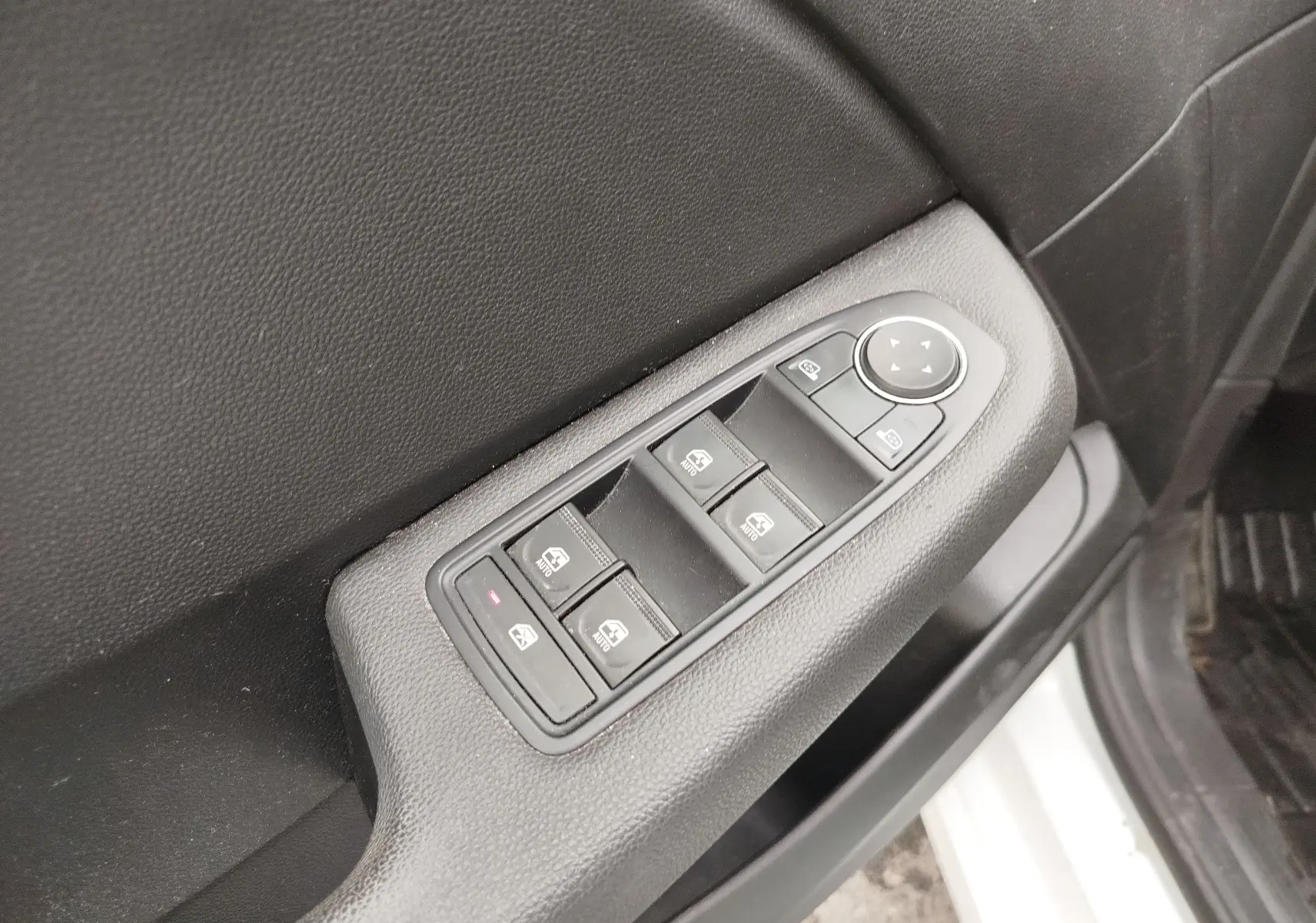 Gros plan sur la commande des vitres électriques côté conducteur d'une Renault Clio blanche, avec boutons noirs et réglage des rétroviseurs.