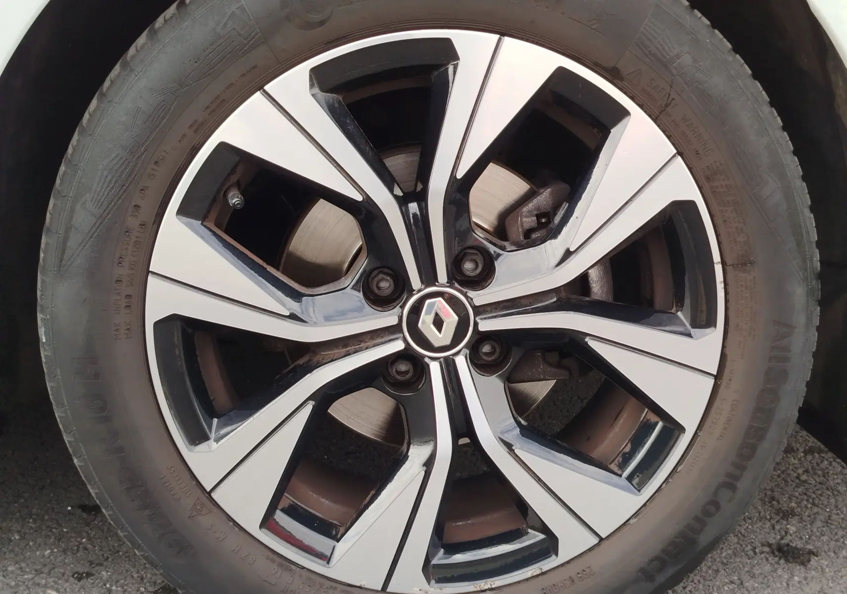 Gros plan sur la jante alliage bicolore noir et argent avec logo Renault au centre d'une Renault Clio Blanc Glacier.