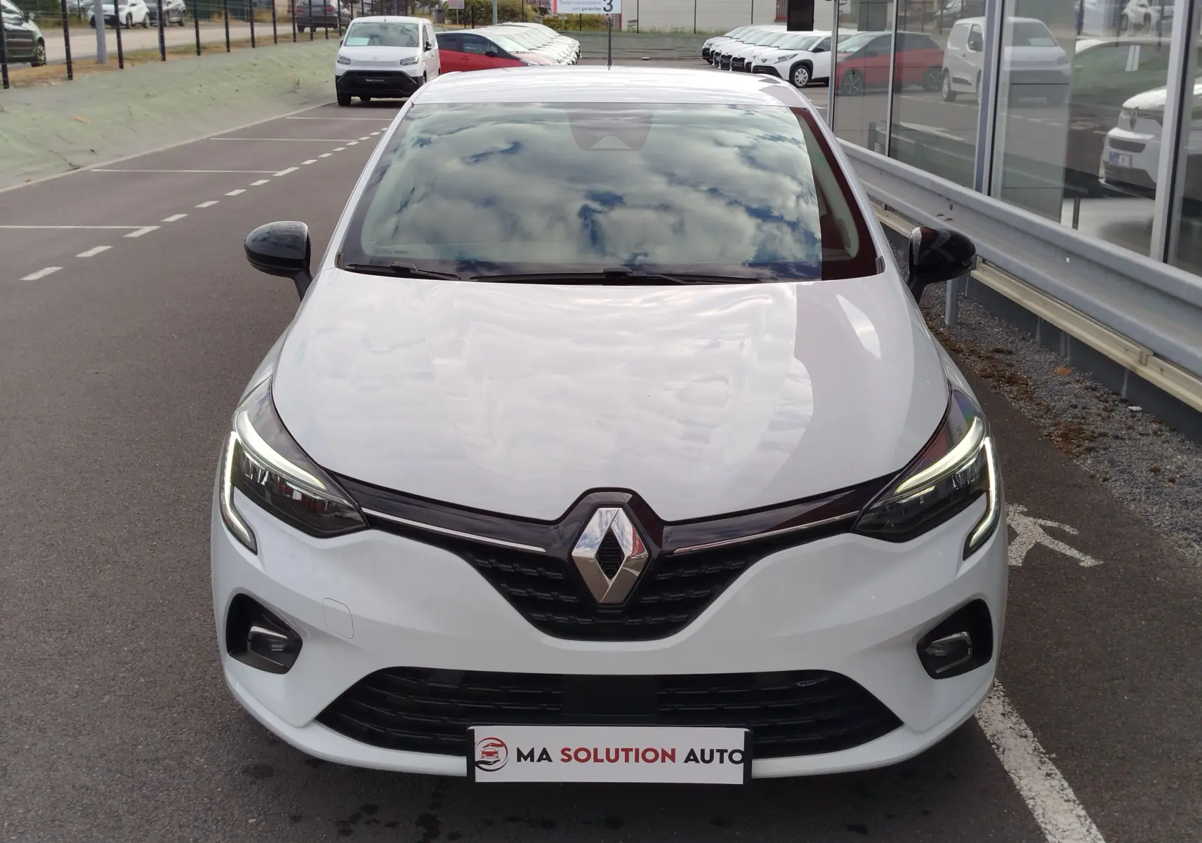 Vue avant d'une Renault Clio 2023 blanc glacier avec phares LED allumés et calandre noire brillante.
