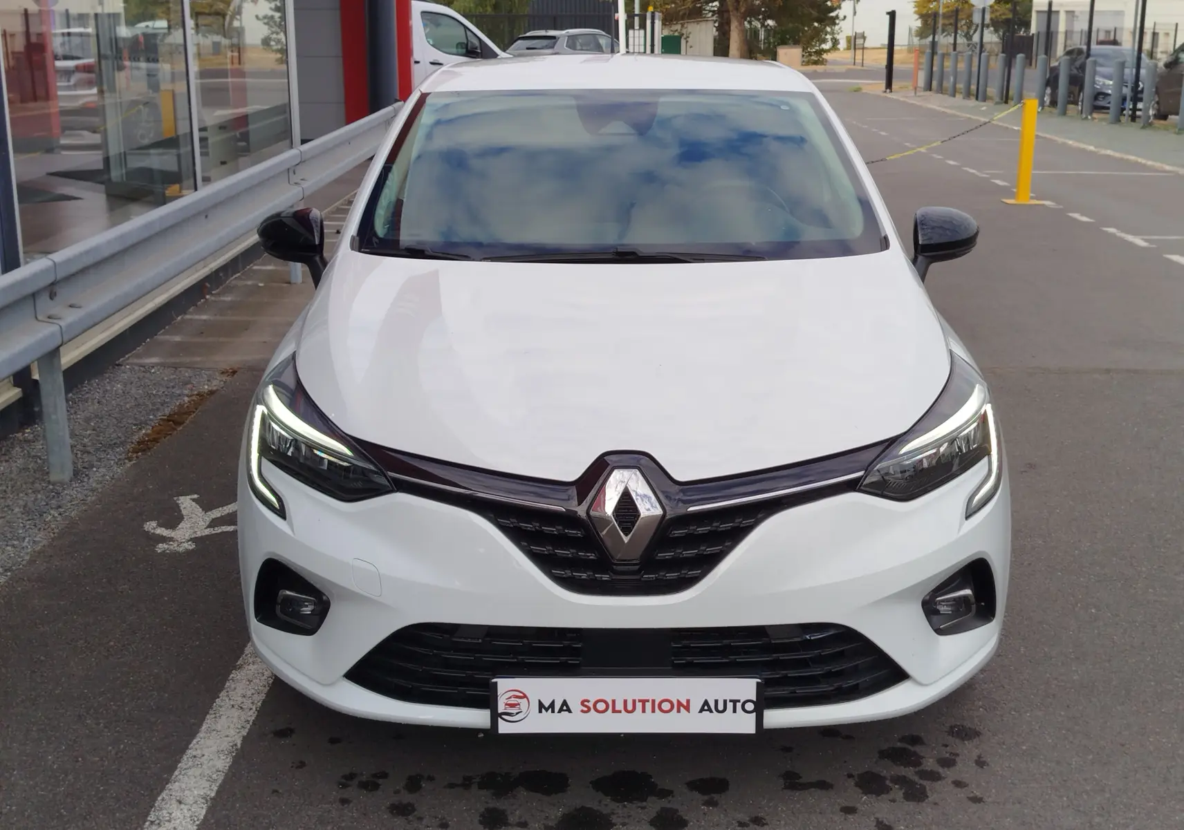 Vue frontale d'une Renault Clio blanche Glacier 2023 avec phares LED allumés et calandre noire brillante.
