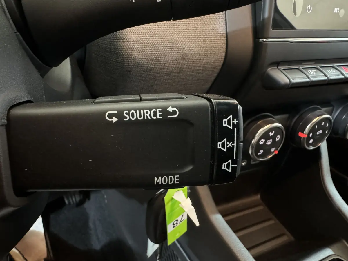 Gros plan sur la commande au volant de la Renault Clio gris clair 2025, avec boutons source et mode visibles.