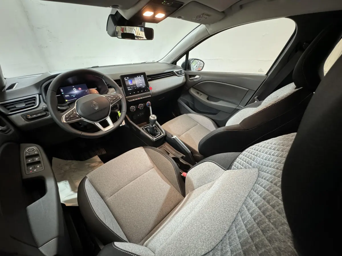 Intérieur avant de la Renault Clio 2025 gris clair, vue côté conducteur, volant cuir multifonctions et écran tactile central visible.