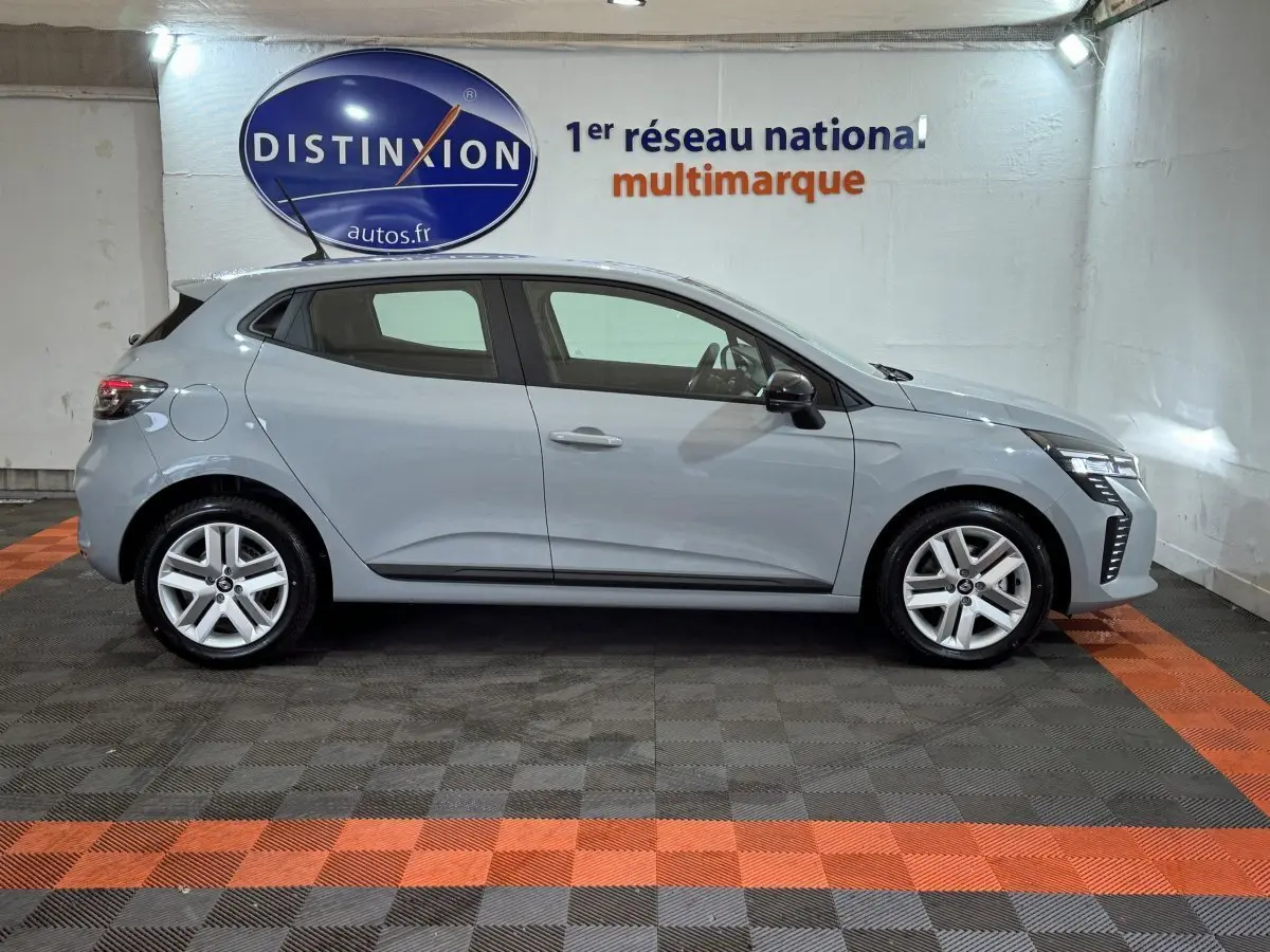 Profil côté droit de la Renault Clio gris clair 2025 avec feux LED et jantes alliage dans un showroom.