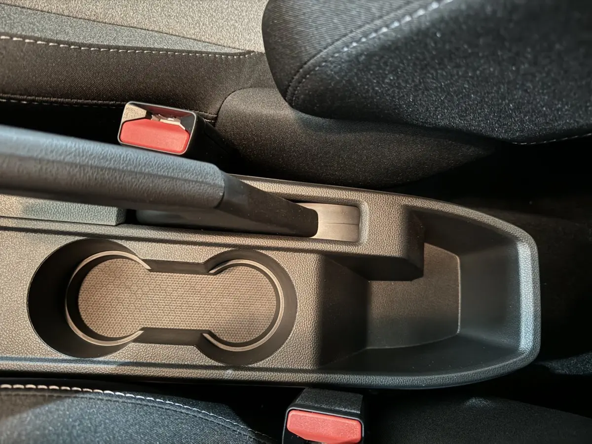Gros plan sur la console centrale noire de la Renault Clio Evolution Blue dCi 100, avec frein à main et deux boutons de ceinture rouges.