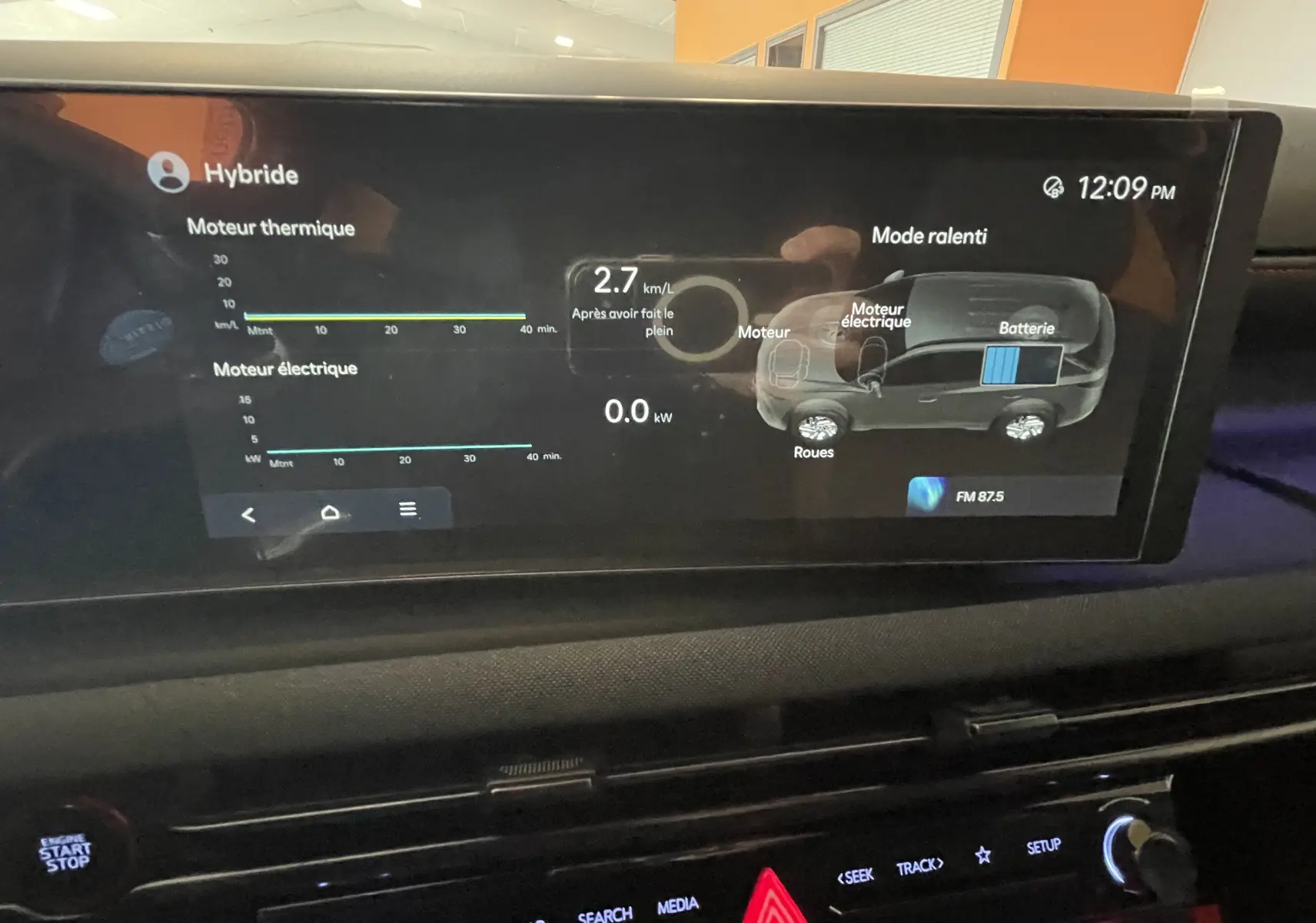 Écran central du Hyundai Tucson 2025 affichant l'état hybride et la consommation en mode ralenti, intérieur noir.