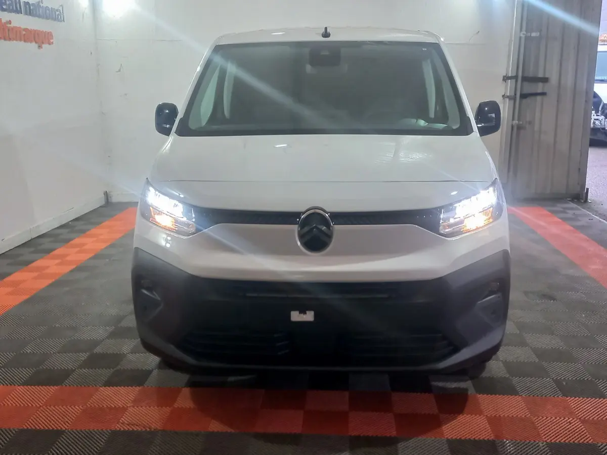 Vue frontale d'un Citroën Berlingo blanc 2025 avec phares allumés et pare-chocs noir dans un garage.