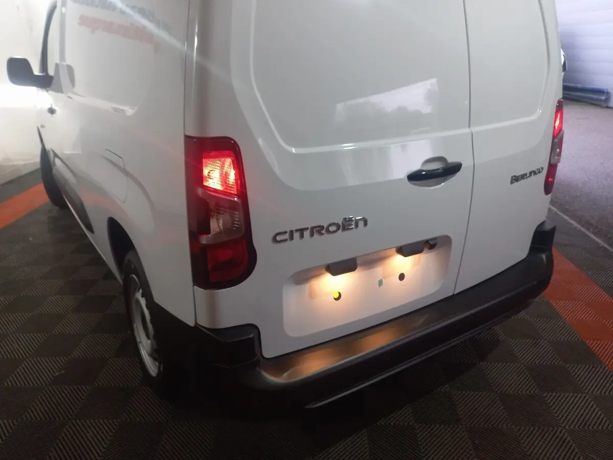 Vue 3/4 arrière gauche d'un utilitaire blanc Citroën Berlingo XL avec feux arrière allumés et porte arrière fermée.