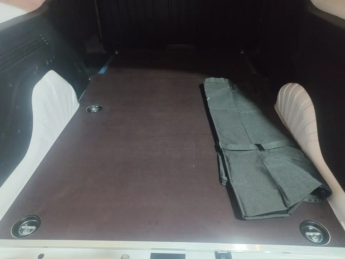 Vue intérieure du coffre du Citroën Berlingo XL blanc 2025, montrant la surface de chargement plane avec un tapis noir partiellement plié.