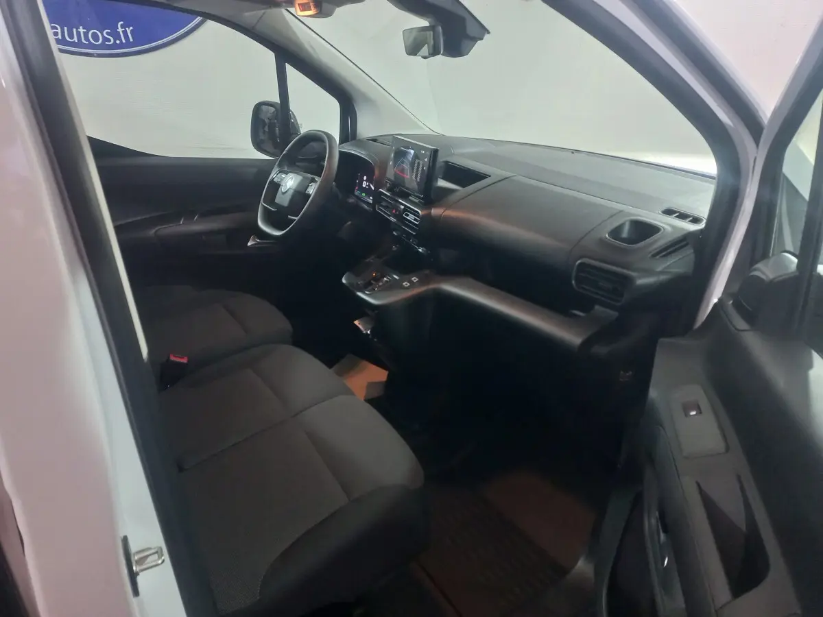 Vue intérieure côté conducteur du Citroën Berlingo blanc 2025, montrant le tableau de bord et les sièges avant noirs.