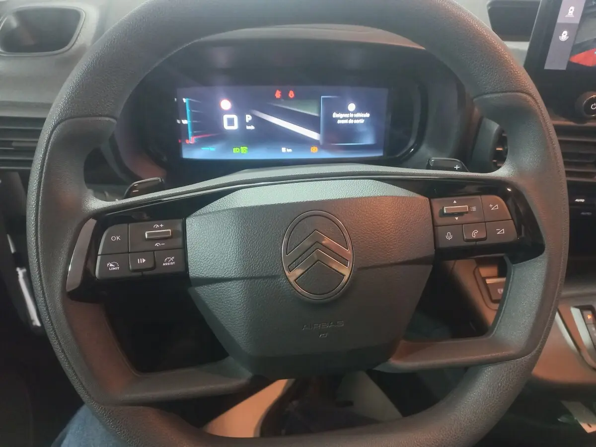 Vue rapprochée du volant multifonctions noir du Citroën Berlingo 2025 avec tableau de bord numérique allumé.