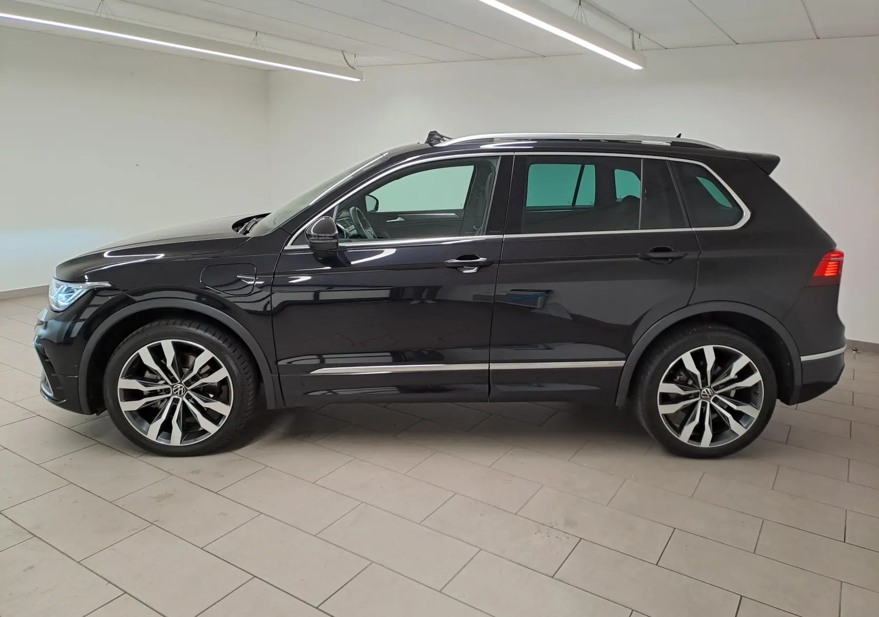 Vue de profil côté gauche d'un Volkswagen Tiguan 1.4 eHybrid noir intense nacré avec jantes 20'' Suzuka et attelage escamotable.