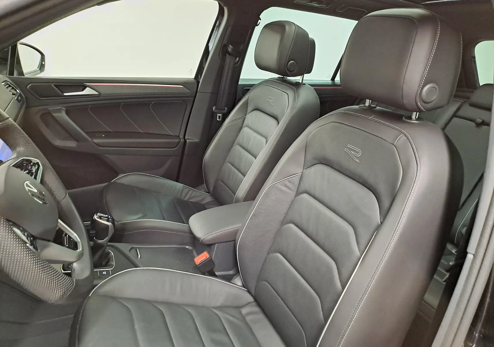 Vue intérieure côté conducteur du Volkswagen Tiguan 1.4 eHybrid 2023 avec sièges cuir noirs embossés "R" et finitions rouges.