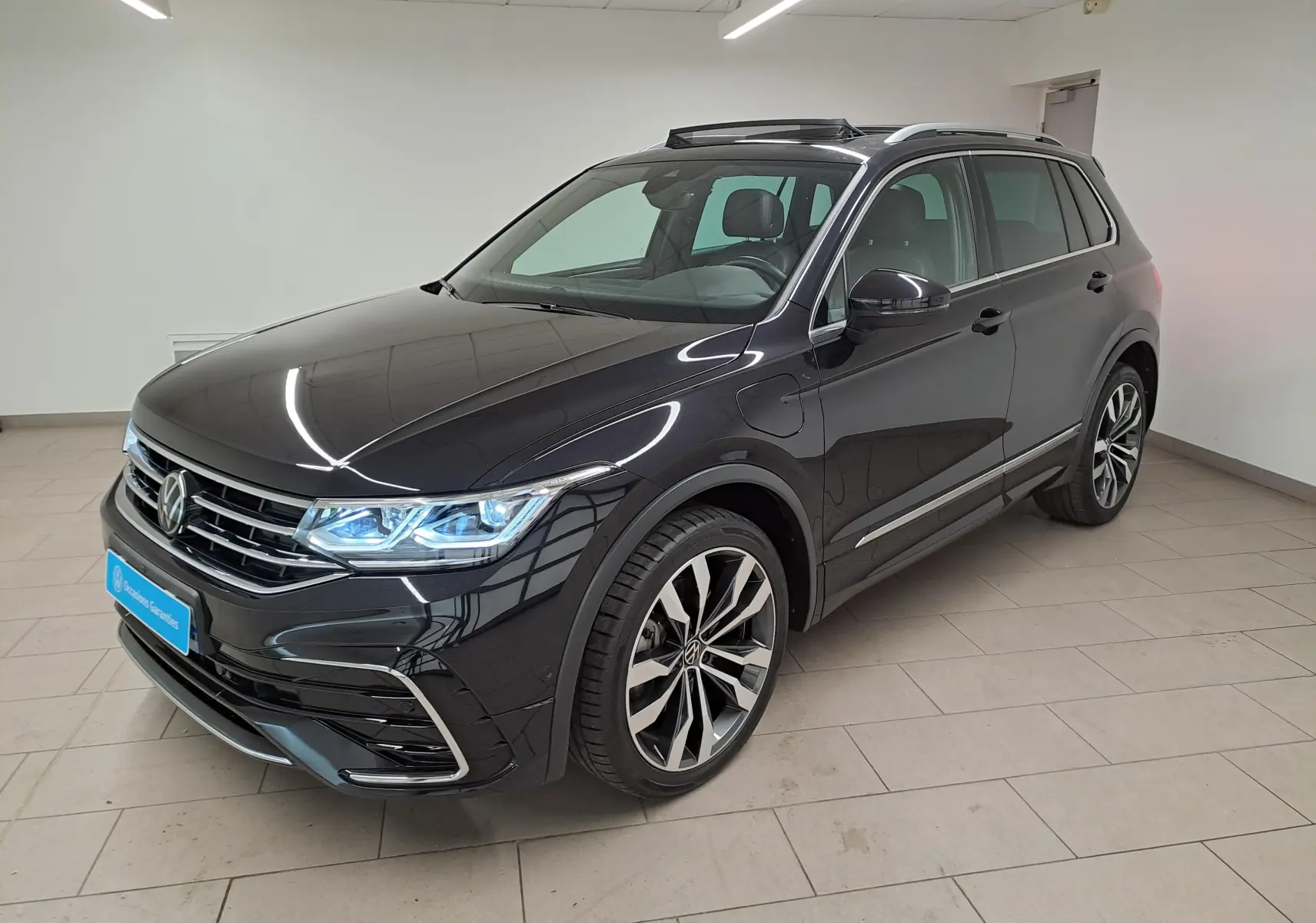 Volkswagen Tiguan 1.4 eHybrid noir intense nacré, vue 3/4 avant droit avec jantes 20'' Suzuka et phares allumés.