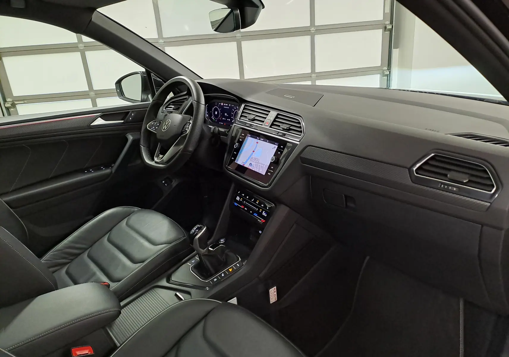 Vue intérieure côté conducteur du Volkswagen Tiguan 2023, tableau de bord noir avec écran tactile et volant multifonction.