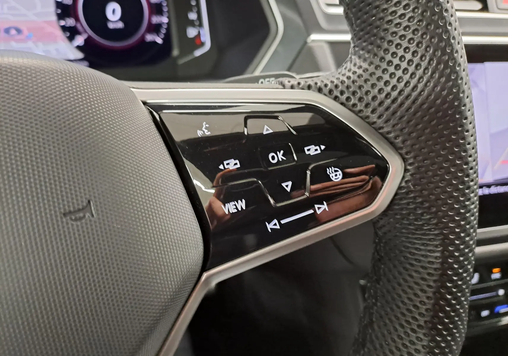 Gros plan sur les commandes multifonctions côté gauche du volant perforé noir du Volkswagen Tiguan 2023 hybride rechargeable.