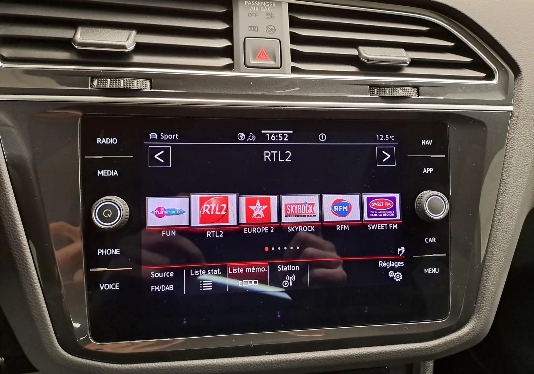 Gros plan sur l’écran tactile central du Volkswagen Tiguan 2023 affichant les stations radio, entouré de commandes noires et grises.