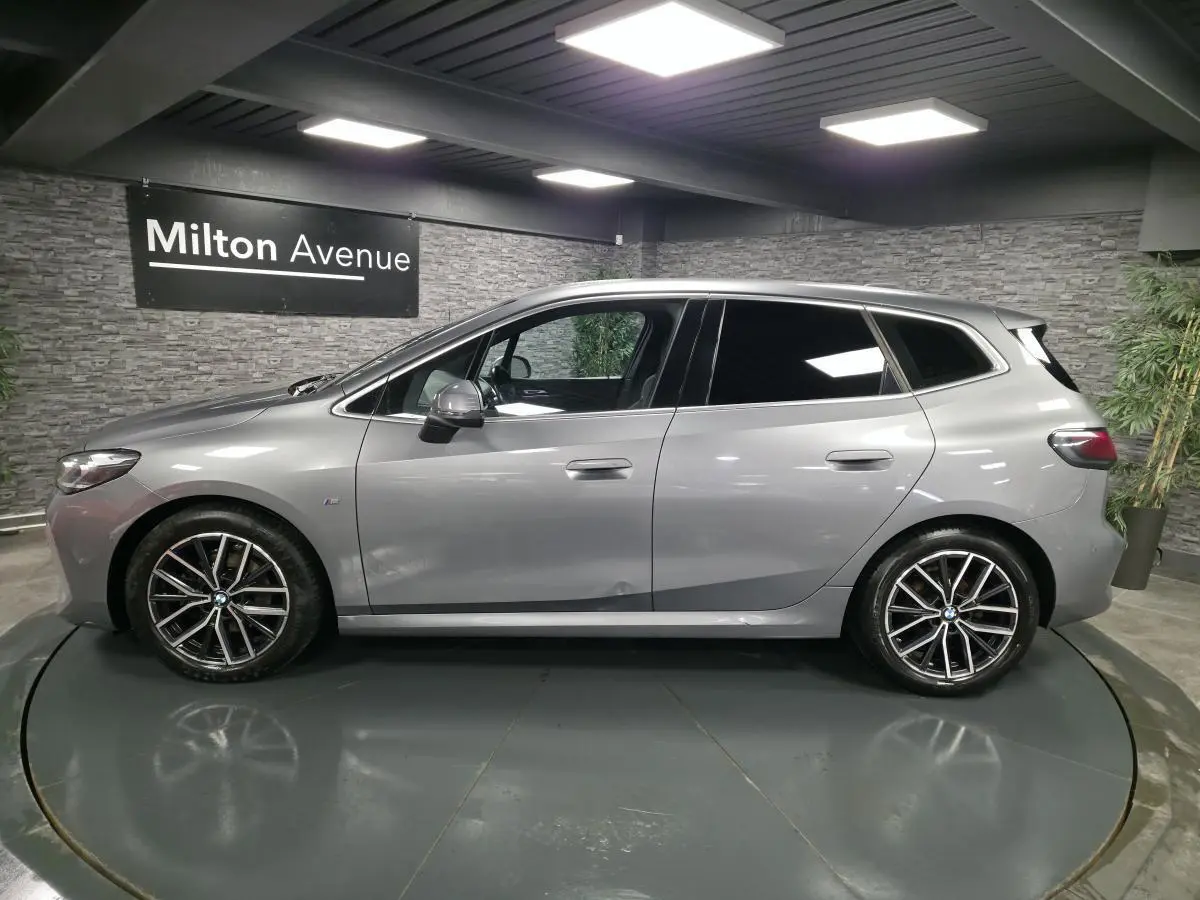 BMW Série 2 218i Active Tourer gris métallisé vue de profil côté gauche avec jantes alliage 18 pouces et vitres teintées.