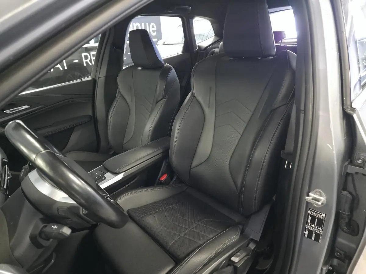 Vue intérieure côté conducteur de la BMW Série 2 218i Active Tourer 2023, sièges sport en similicuir noir et console centrale grise.