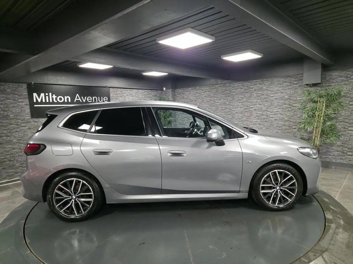 BMW Série 2 218i Active Tourer gris métallisé vue de profil côté gauche en intérieur showroom.