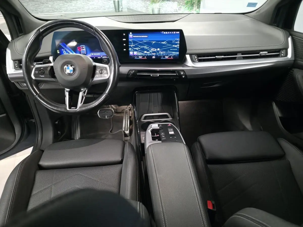 Vue intérieure avant de la BMW Série 2 218i Active Tourer 2023, tableau de bord numérique et volant cuir M noir.