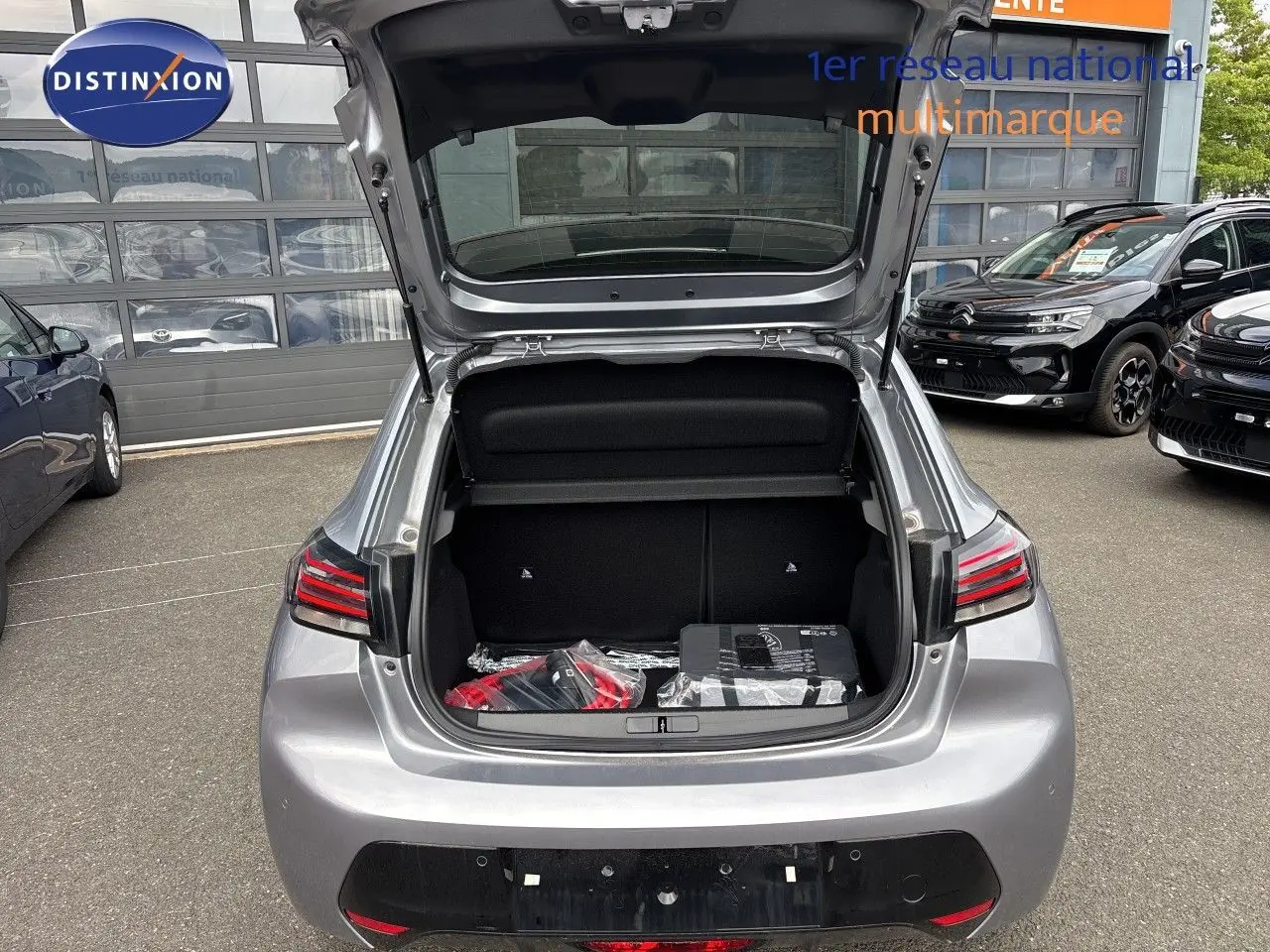 Vue arrière ouverte sur le coffre d'une Peugeot 208 électrique 2026 gris Artense métal, avec accessoires visibles à l'intérieur.