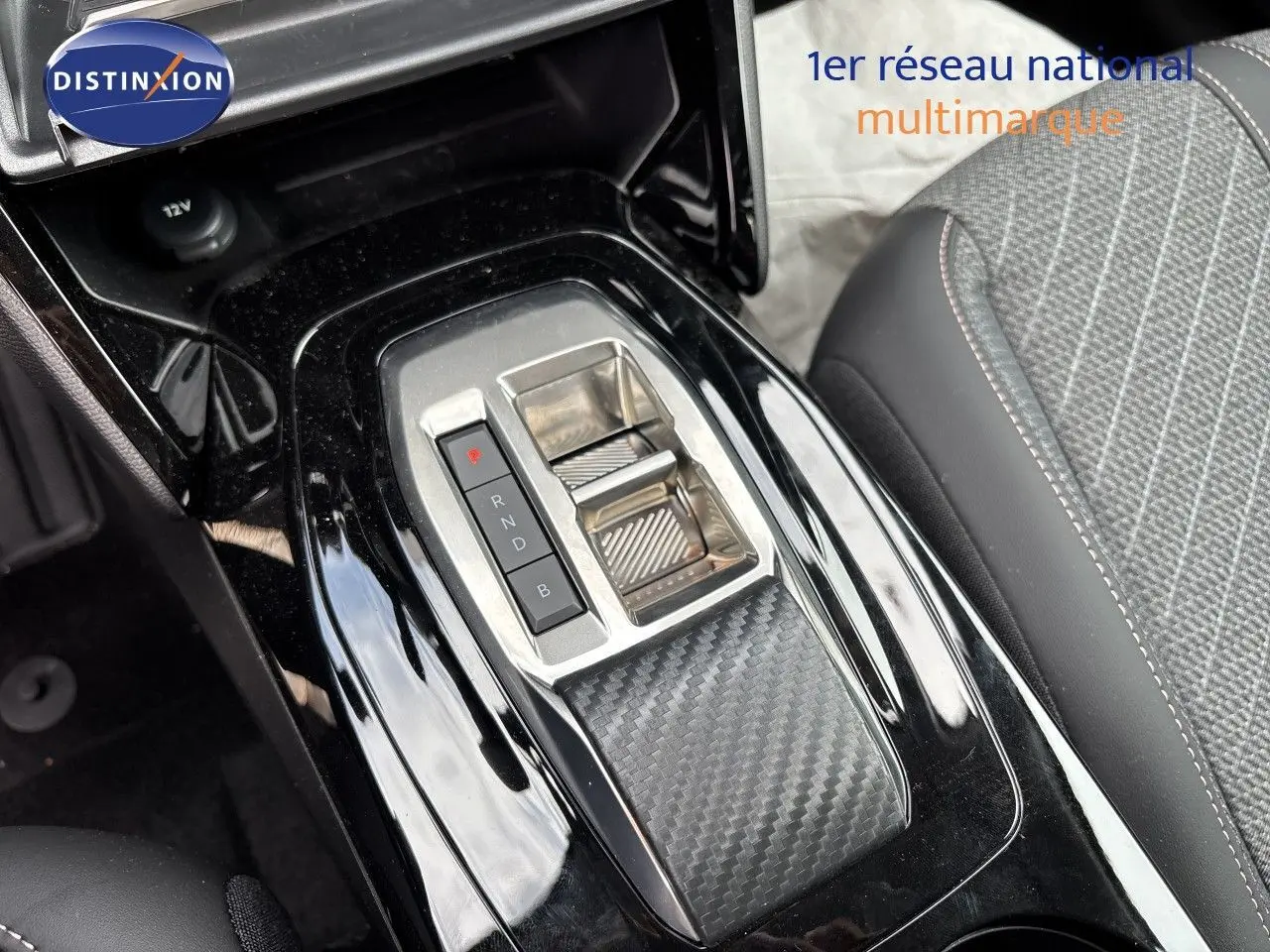 Gros plan sur la console centrale noire brillante avec sélecteur de vitesses électrique et siège tissu gris de la Peugeot 208 électrique.