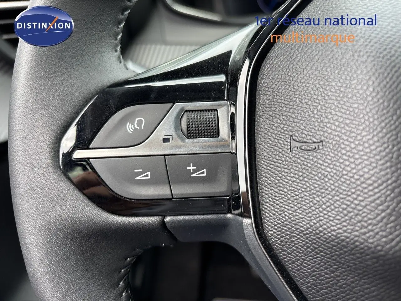 Gros plan sur les commandes gauche du volant cuir noir d’une Peugeot 208 électrique gris Artense, avec boutons de volume et téléphone.