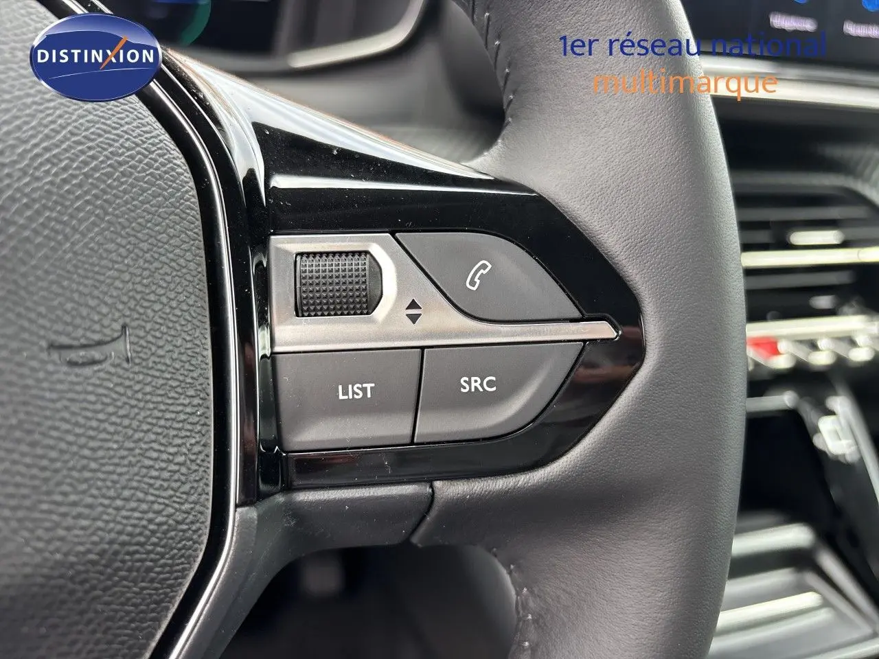 Gros plan sur les commandes gauche du volant cuir noir de la Peugeot 208 électrique gris Artense, avec boutons fonction audio et téléphone.