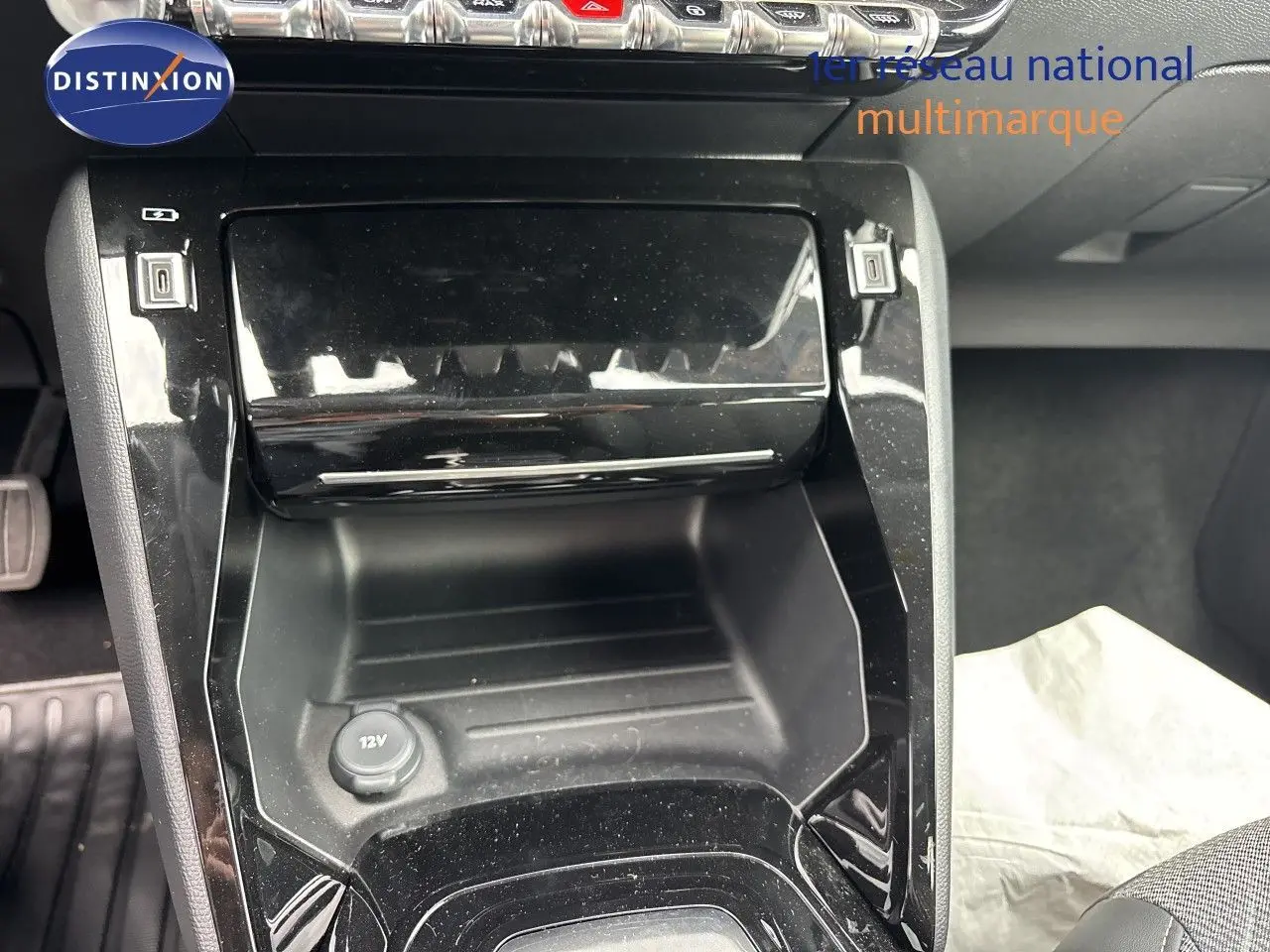 Gros plan sur la console centrale noire brillante de la Peugeot 208 électrique 2026, avec prise 12V visible.