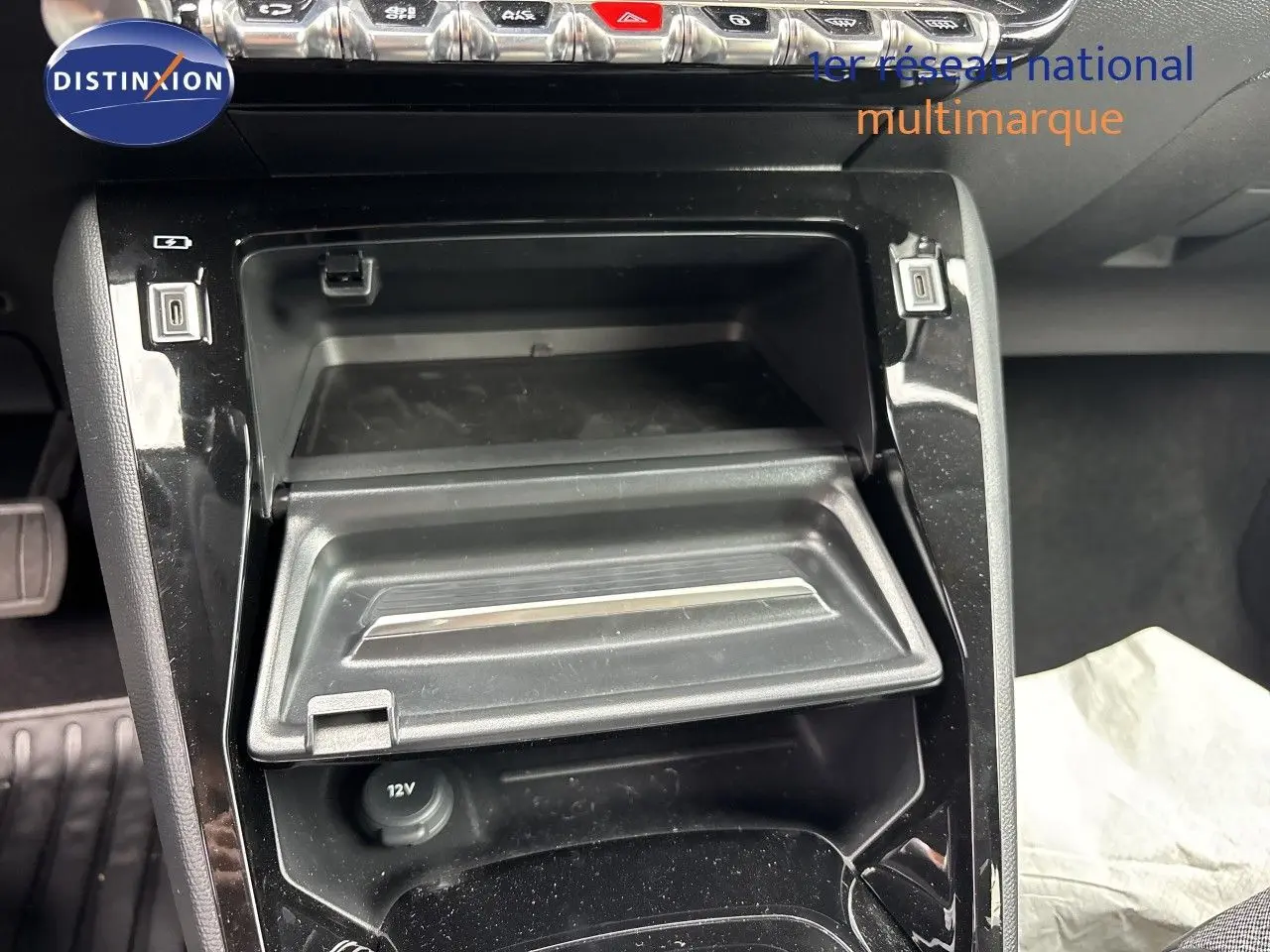 Gros plan sur la console centrale de la Peugeot 208 électrique 2026, avec rangement ouvert et prises USB visibles.