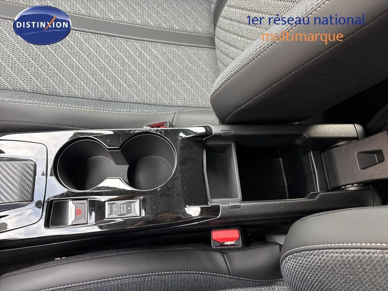Vue rapprochée de la console centrale noire brillante avec porte-gobelets et accoudoir, sièges tissu gris et cuir noir Peugeot 208 électrique.