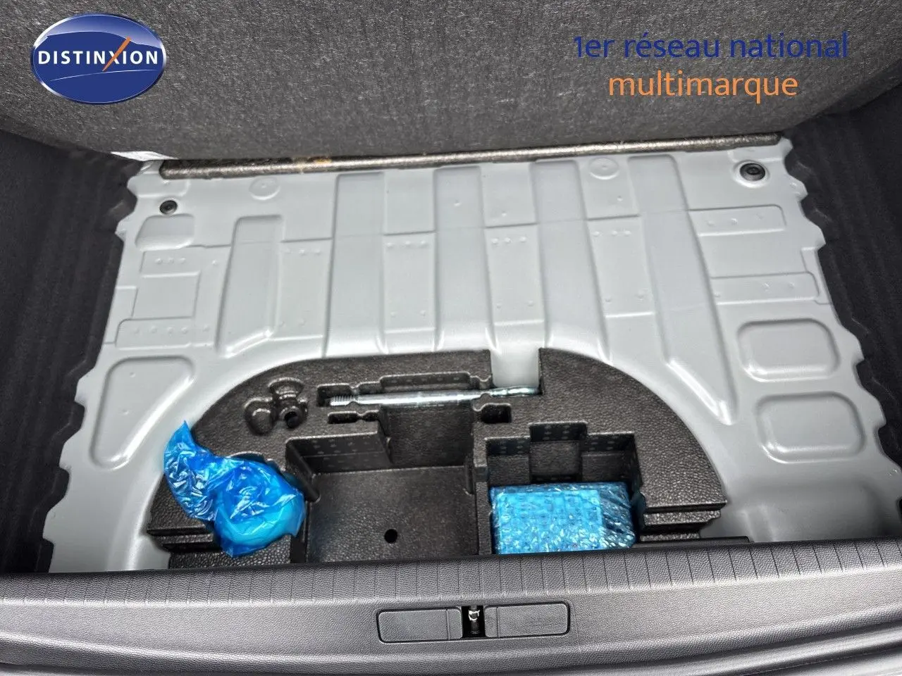 Coffre ouvert d’une Peugeot 208 électrique gris Artense, vue plongeante sur le rangement sous plancher avec outils emballés.