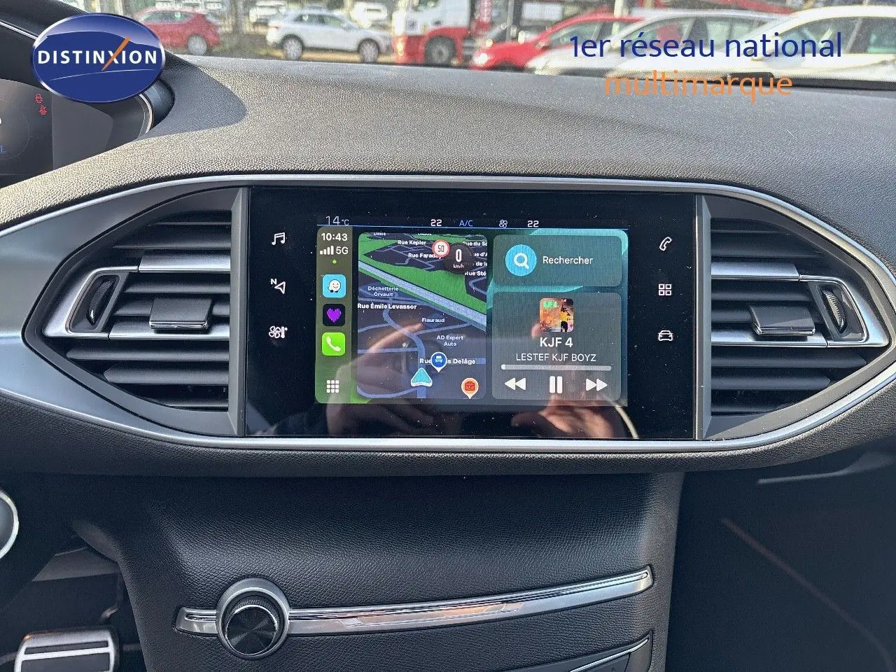 Écran tactile central avec navigation et musique dans l'habitacle d'une Peugeot 308 blanche nacrée, vue de face.