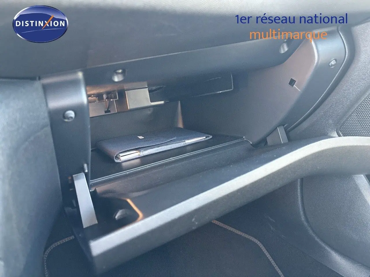 Gros plan sur la boîte à gants ouverte du Peugeot 308 blanc nacré, montrant un carnet à l'intérieur.