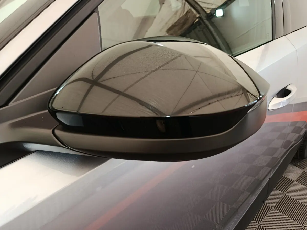 Rétroviseur côté gauche noir brillant sur Peugeot 3008 gris clair, avec reflet de l'environnement intérieur.