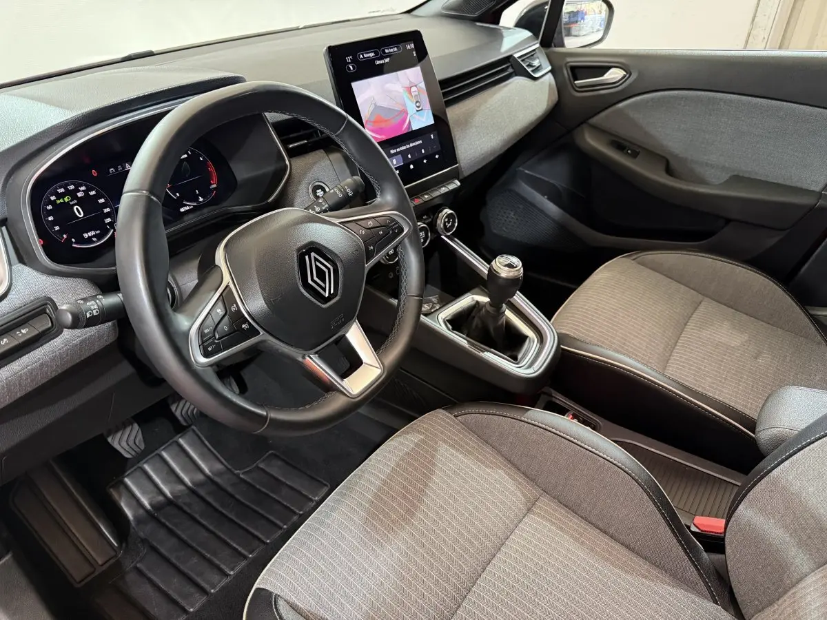 Intérieur Renault Clio Techno TCe 90 2024 vu côté conducteur, volant cuir, écran tactile vertical et sièges gris.