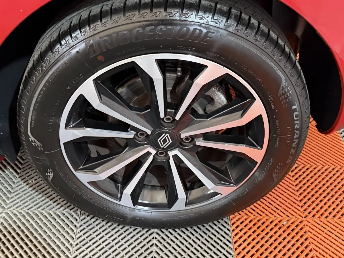 Gros plan sur la roue avant droite d'une Renault Clio rouge 2024 avec jante alliage noire et argentée au design moderne.